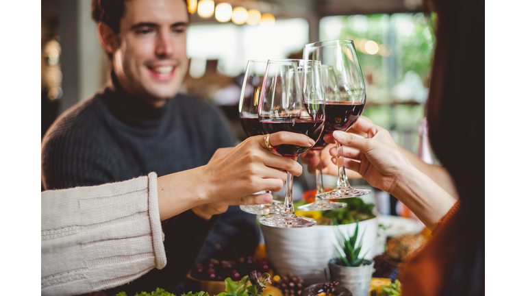 Group of young people celebrating Christmas party dinner with clinking glass of wine