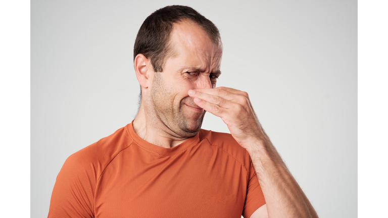 Caucasian man is pinching nose with fingers and looking with disgust because of bad smell isolated on white background