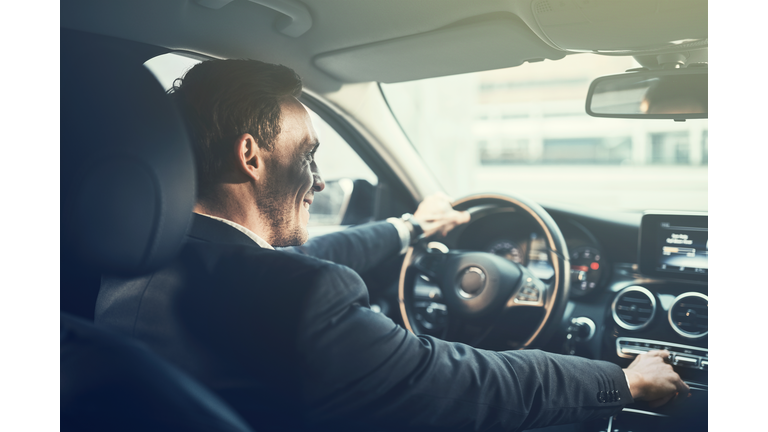 Smiling young businessman changing radio stations while driving his car