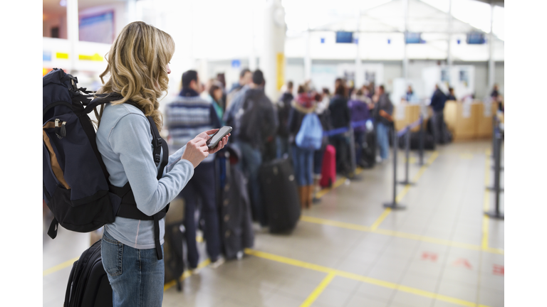 female traveller texting at airport check-in desk