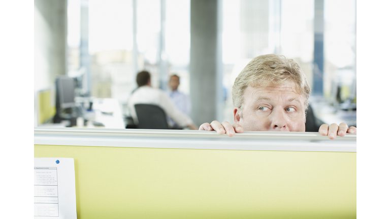 Businessman peering over cubicle wall