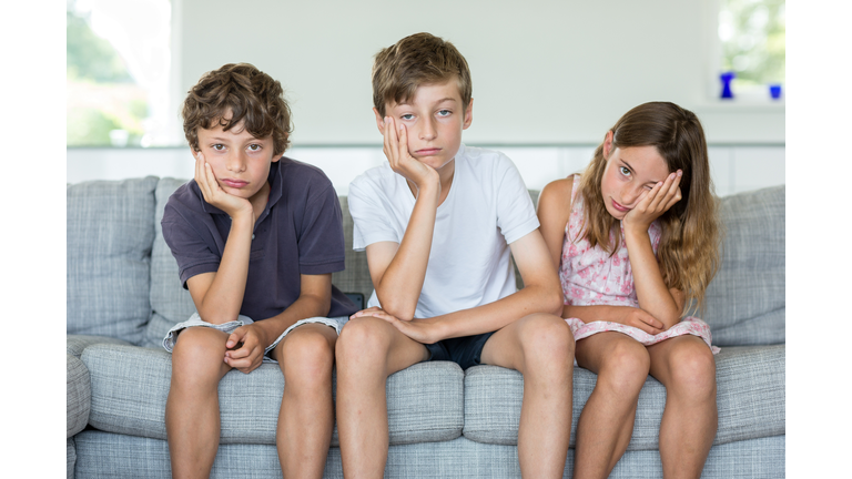 Brothers and sister on sofa looking bored