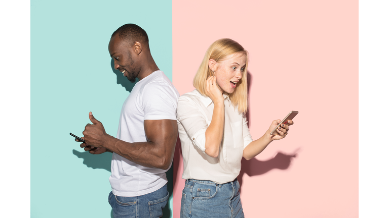 Mixed raced couple of students taking mobile phones. Caucasian girl and her African boyfriend posing at studio