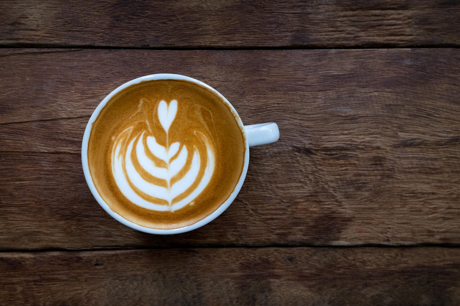 A white cup of hot latte art coffee on the wooden table in coffee shop