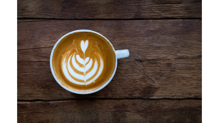 A white cup of hot latte art coffee on the wooden table in coffee shop