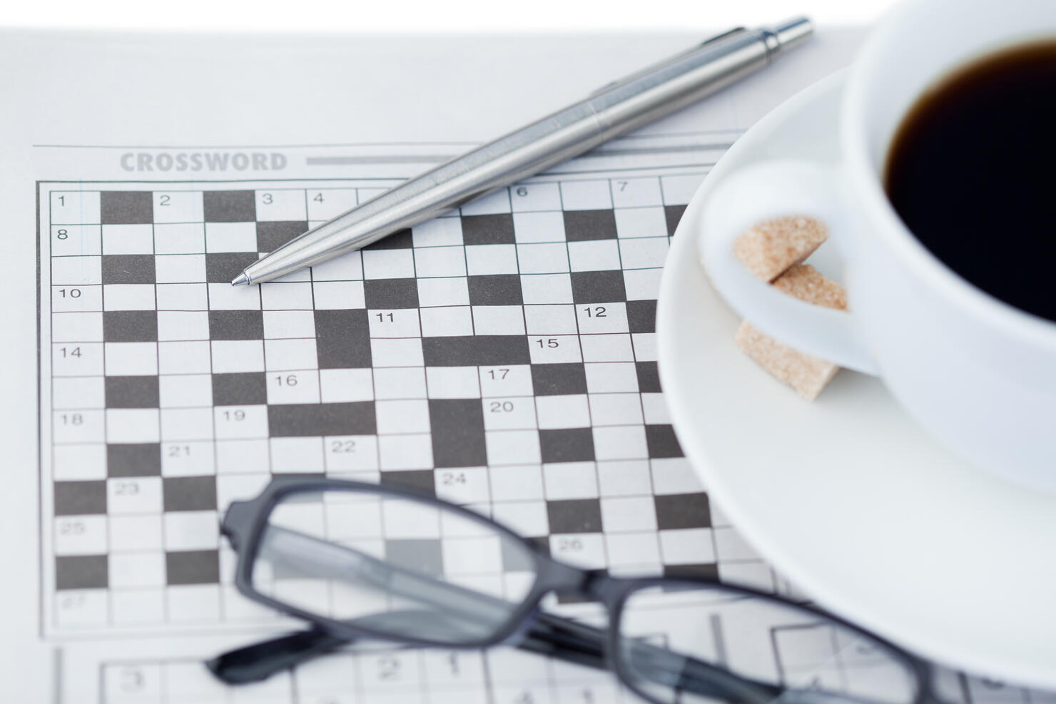 A cup of coffee a pen a pair of glasses and a crossword puzzle