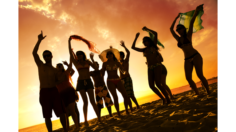 Spring break backlit group of young people dancing on beach