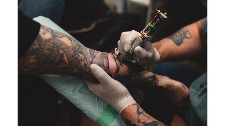 Tattooist tattooing young mans arm, close-up