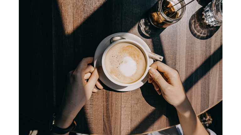 Top view of woman sitting by the window in coffee shop enjoying the warmth of sunlight and drinking coffee