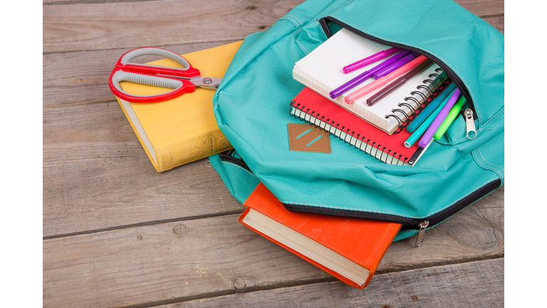 Backpack and school supplies: books, notepad, felt-tip pens, scissors on brown wooden table