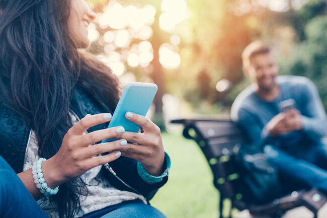 Flirting couple in the park texting on smartphones
