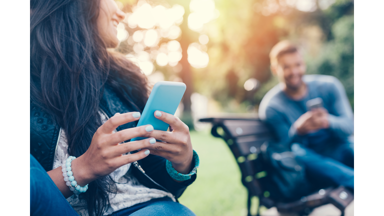 Flirting couple in the park texting on smartphones