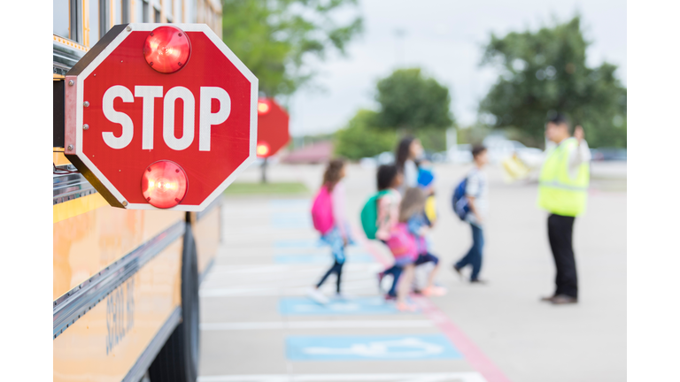 Lights flash on a school bus stop sign as children cross street