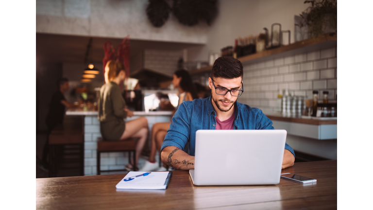 Young hipster businessman working on laptop at urban coffee shop