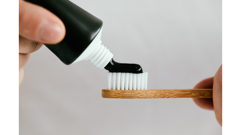 Male hands with a black toothpaste and a bamboo toothbrush