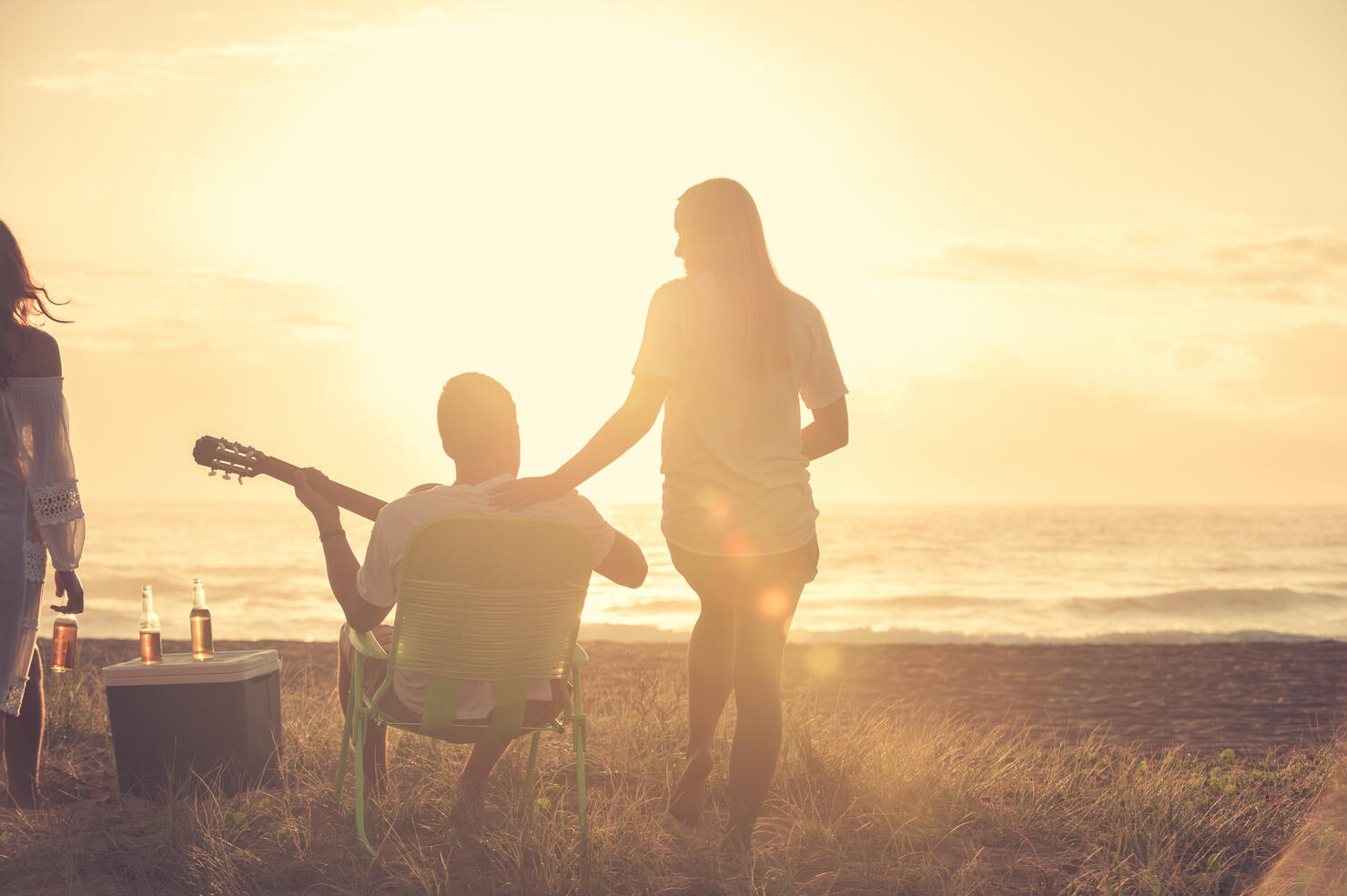 Young couple on beach looking at sunset with guitar.