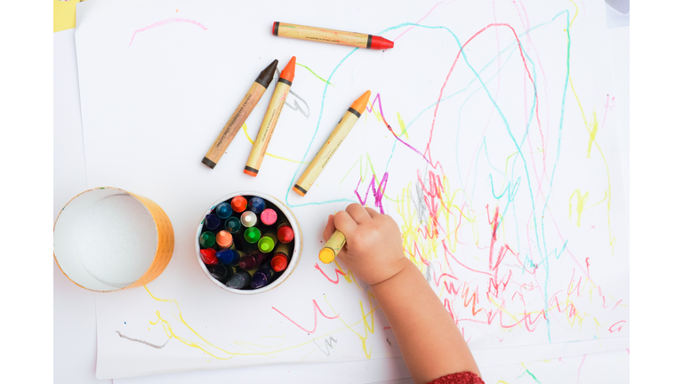 Baby's hand drawing on the white paper with colorful crayons