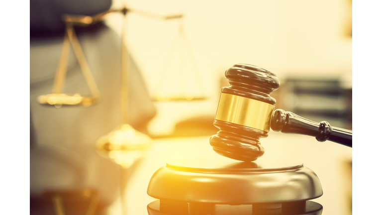 Legal office of lawyers, justice and law concept : Wooden judge gavel or a wood hammer and a soundboard used by a judge person on a desk in a courtroom with a blurred brass scale of justice behind.