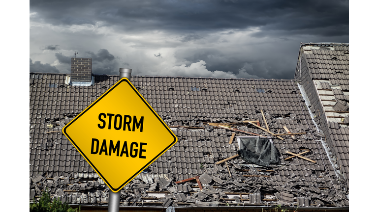 yellow damage warning sign in front of storm damaged roof of house