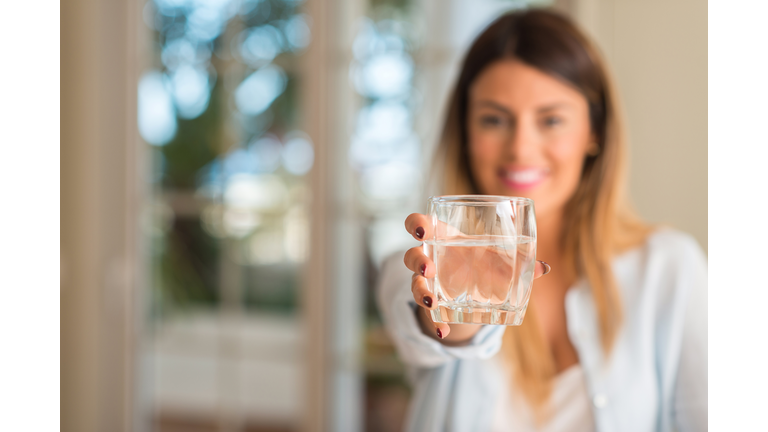 Beautiful young woman smiling while holding a glass of water at home. Lifestyle concept.