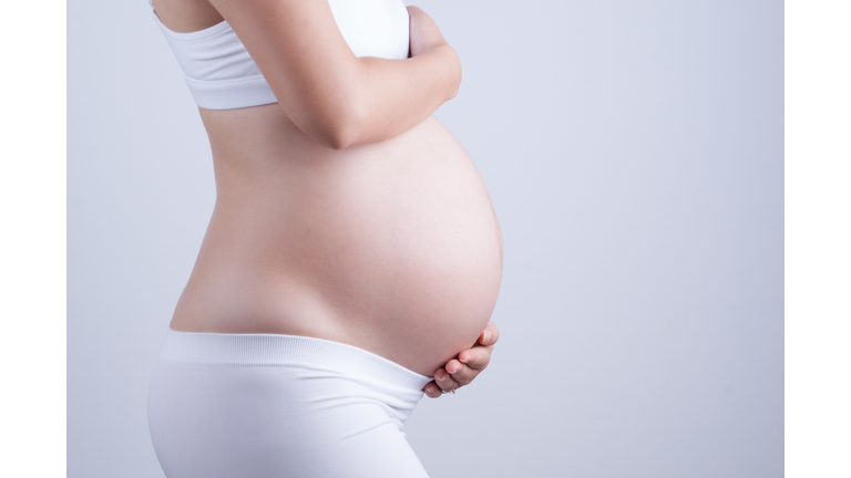 Midsection Of Pregnant Woman Touching Belly By Gray Background