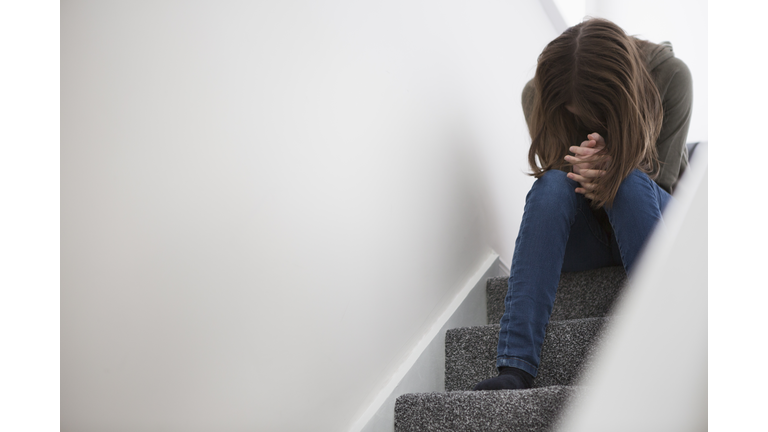 Teenage girl sitting on stairs with head down in despair