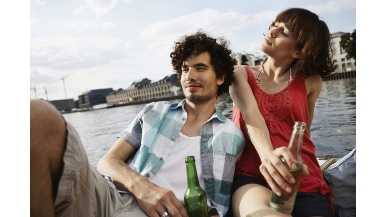 Germany, Berlin, Young couple on motor boat, holding bottles, portrait, close-up