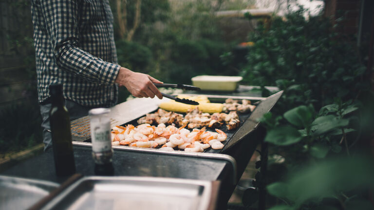 Holding tongs grilling prawns, meat and vegetables on barbecue