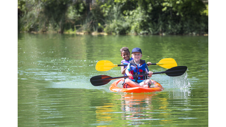 Two diverse little boys kayaking down a beautiful river