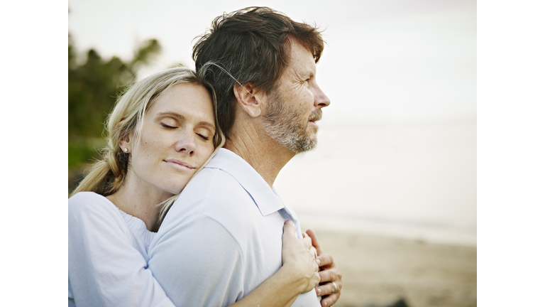 Wife embracing husband on beach at sunset