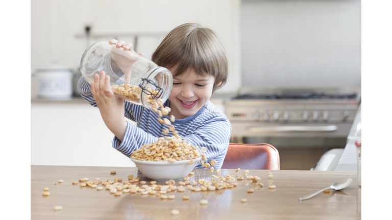 Boy pouring cereal into bowl in kitchen