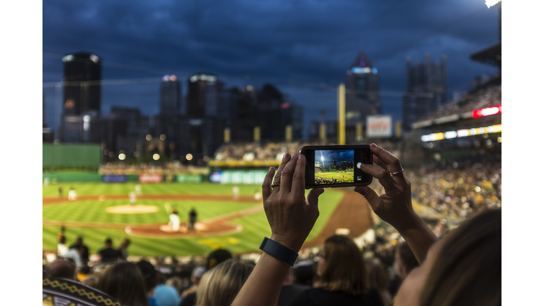 Hands of woman photographing baseball game with cell phone