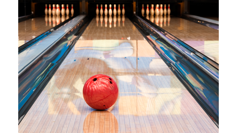 Red bowling ball sitting in middle of newly oiled lane