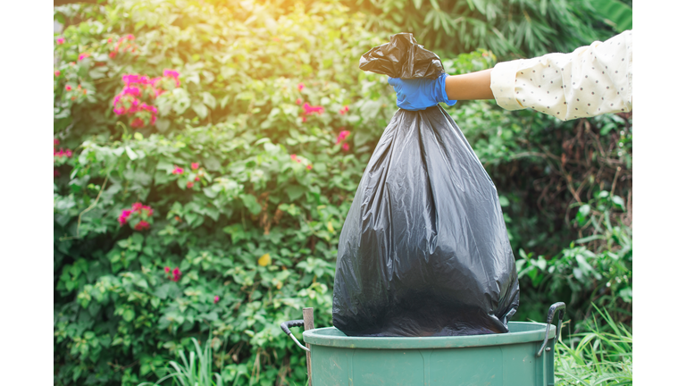 Cropped Image Of Volunteer Holding Garbage Bag Over Can Against Trees
