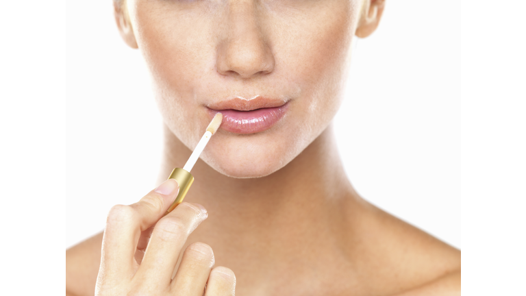 Studio portrait of beautiful woman applying lip gloss