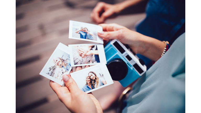Young woman holding polaroid photos with mum on summer holidays