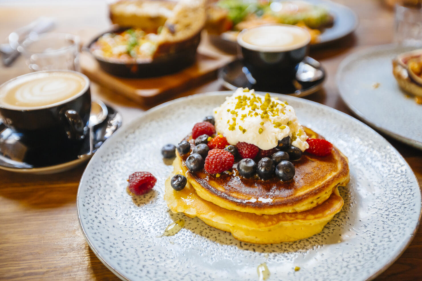Stack of pancakes with fresh blueberry, raspberry and ricotta cheese on a plate, served with coffee in cafe