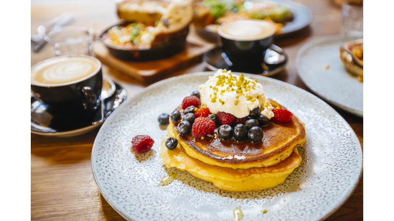 Stack of pancakes with fresh blueberry, raspberry and ricotta cheese on a plate, served with coffee in cafe