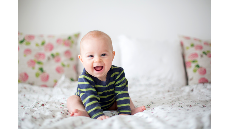 Cute little four month old baby boy, playing at home in bed in bedroom, soft back light behind him