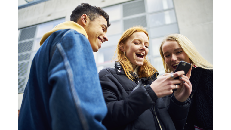 Three teens laughing and joking while looking at their phone