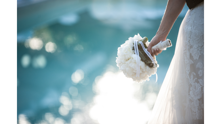 Midsection Of Bride Wearing Wedding Dress While Holding Bouquet By Swimming Pool