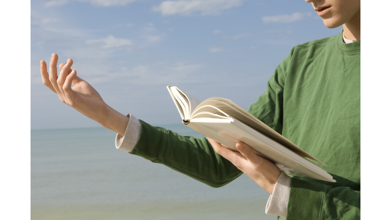 Young male reading aloud from book at the beach