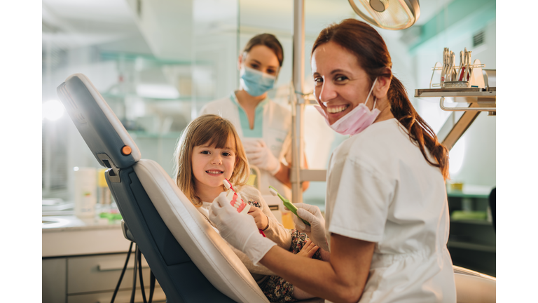 Happy little girl at dentist's office learning how to brush teeth.