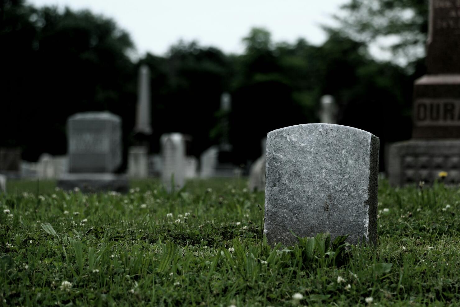 Tombstones On Grassy Field In Cemetery Against Sky