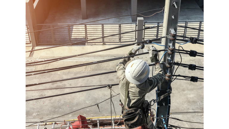 Rear View Of Electrician Repairing Power Lines