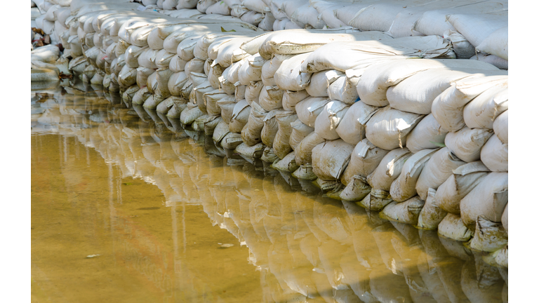 White sandbags for flood defense and it's reflection brown water