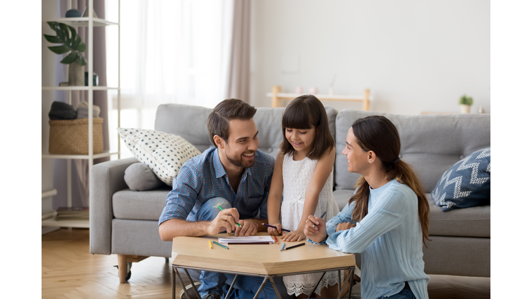 Caring mom and dad teaching little daughter to draw