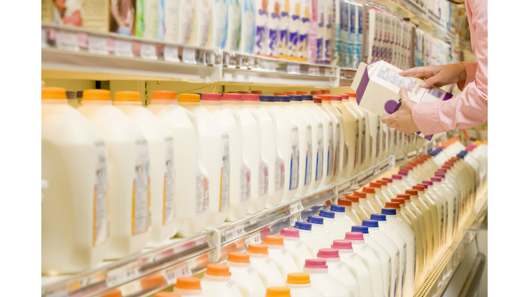 Woman checking ingredients on back of milk carton in supermarket