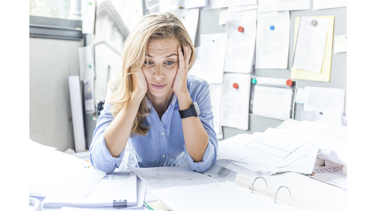 Stressed woman sitting at desk in office surrounded by paperwork