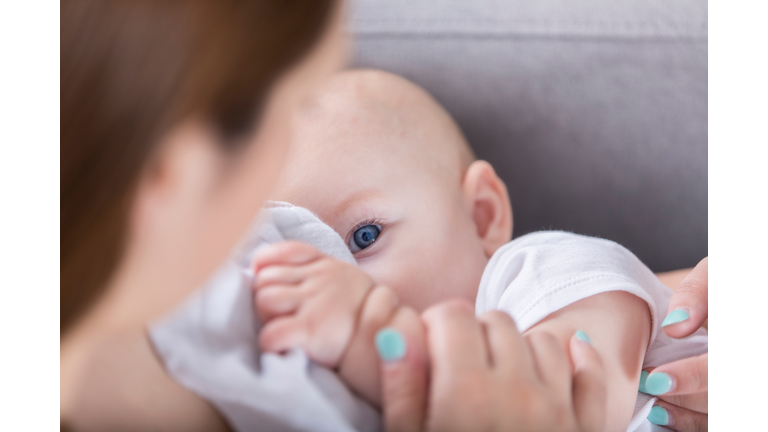Adorable blue eyed baby looks at mom while breastfeeding